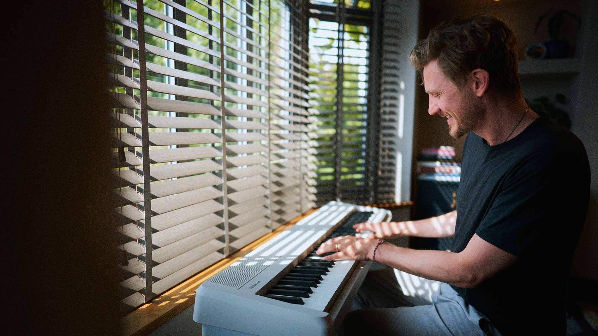 A man sat by a window playing the Roland FP-40 digital piano 