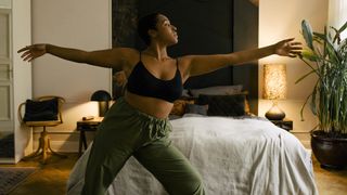 A woman stands in front of her bed doing yoga poses