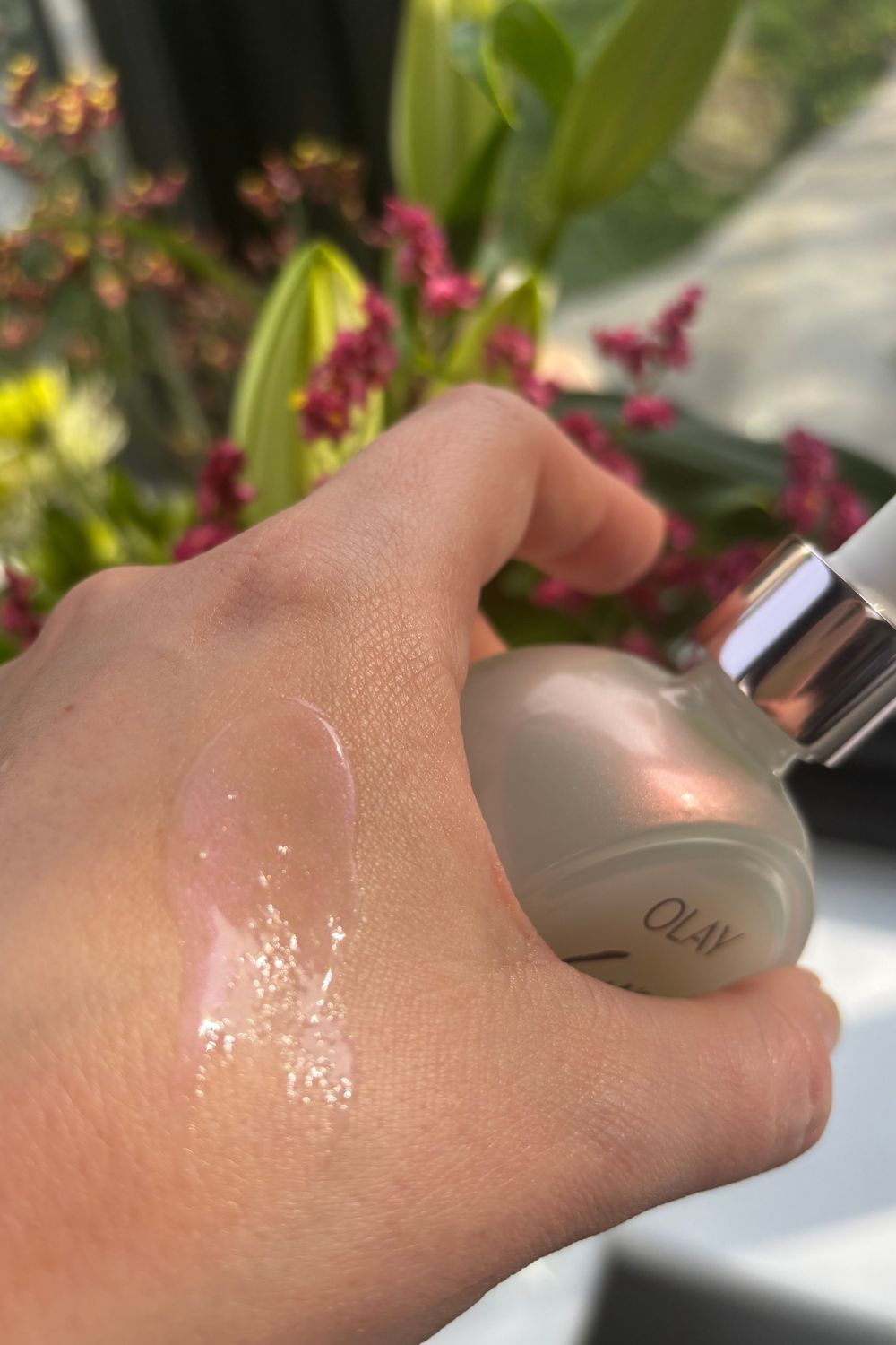 a hand holding a bottle of olay super serum with a smear of product