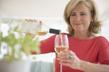 a woman in a red shirt pours a glass of white wine