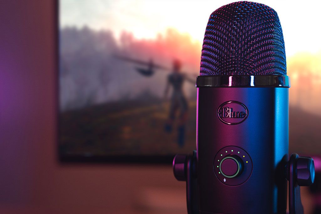 Close up of blue yeti mic in front of gameplay of a generic fantasy game on a monitor. 