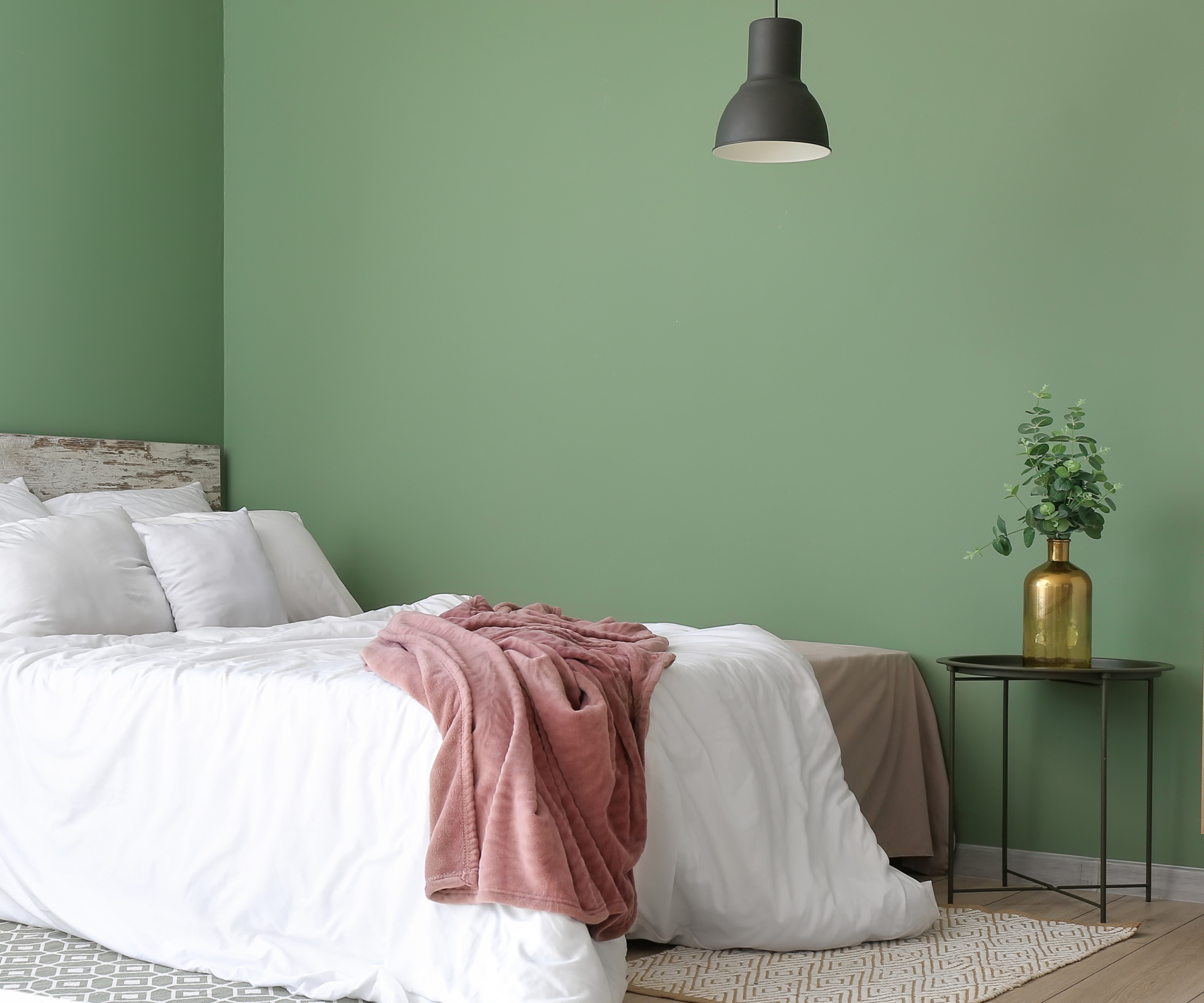 bedroom with green painted walls, bed with white bed linen and pink throw, black ceiling pendant light and small round table with vase and plants