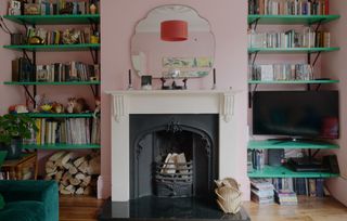 Colourful living space with fire place, pink walls and green shelves at Forest House