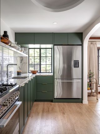 A kitchen with dark green cabinets and white backsplash