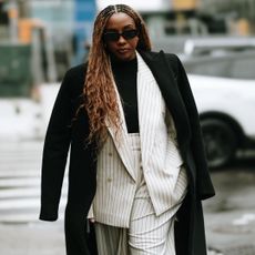 new york fall winter 2025 fashion week attendee wearing sunglasses black coat and white pinstripe suit