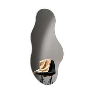 A wavy mirror with a reflection of a gray room with a black chair with a beige throw draped over the top of it