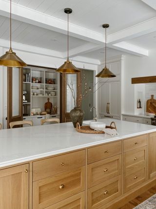 A modern kitchen with white cabinetry and a wooden island with a marble countertop with three gold pendant lights above