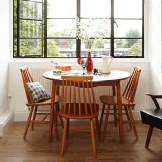 small dining area in window, round retro style table, with matching chairs. retro tableware, glass vase, pitcher, crittall window, cushion on one chair
