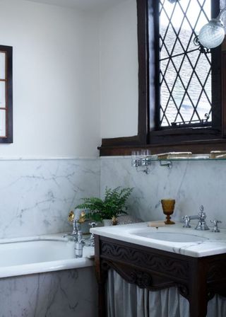 Farmhouse bathroom with marble splashback and sink, with dark wooden fittings