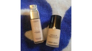 A close-up of the L'Oreal Paris True Match Foundation alongside the Armani Luminous Silk Foundation, on top of a blue and white blanket