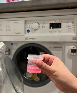 A capful of pink laundry detergent in front of a washing machine set to delicate