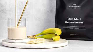 Protein Works Diet Meal Replacement shake packaging next to 2 bananas and a glass full of the shake.