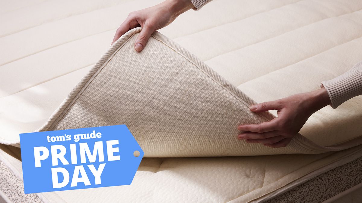 A pair of hands lifting the Birch Plush Organic Mattress Topper off the surface of the Birch Natural Mattress, a Tom&#039;s Guide Prime Day deals graphic (left)