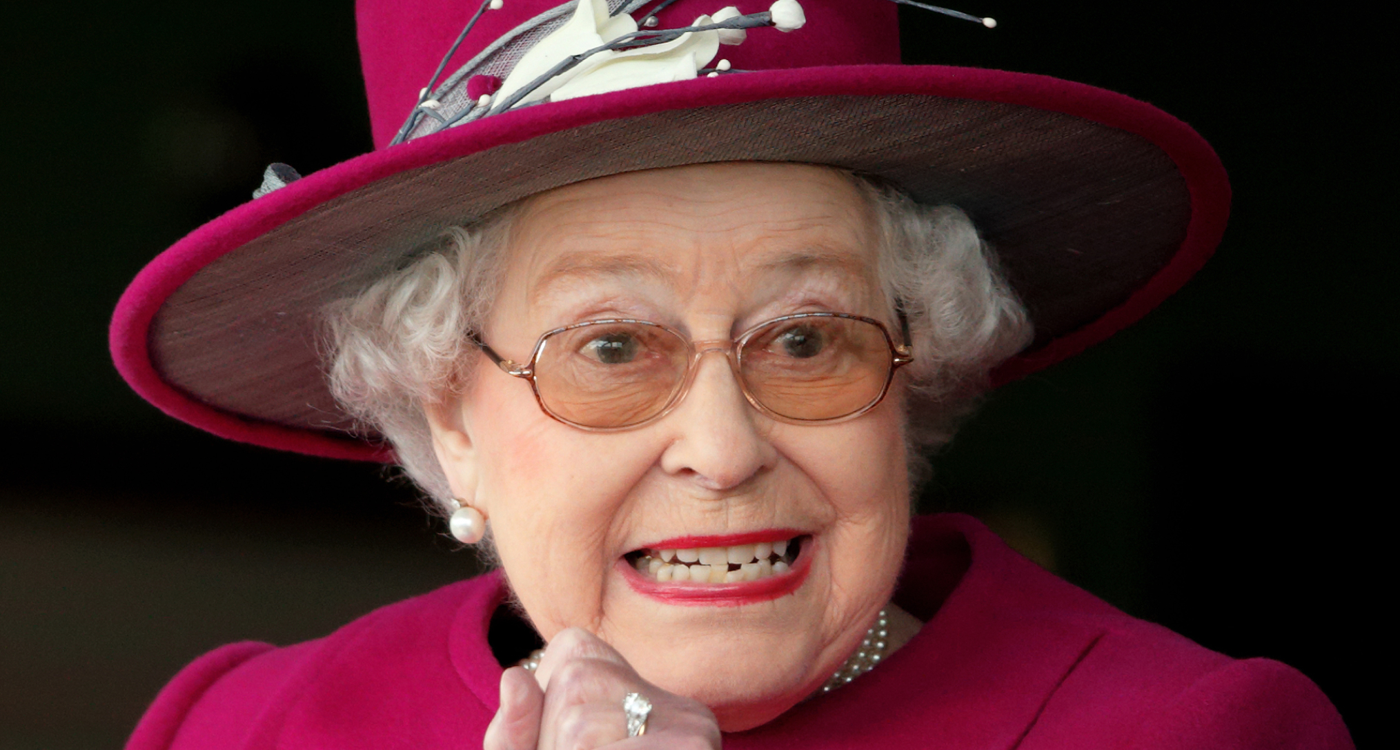 Queen Elizabeth gritting her teeth in a pink hat and coat