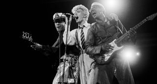 A black-and-white image of David Bowie flanked by bassist Carmine Rojas on the the left, and Carlos Alomar on the right.