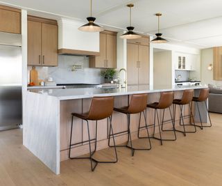 A wood and white kitchen with statement pendants over the island and brown leather counter stools