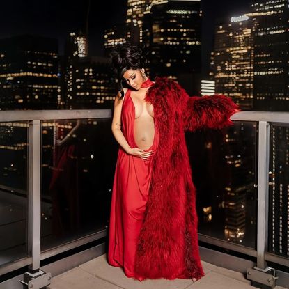 Cardi B wears a belly baring red gown with a red fur coat to announce her third pregnancy