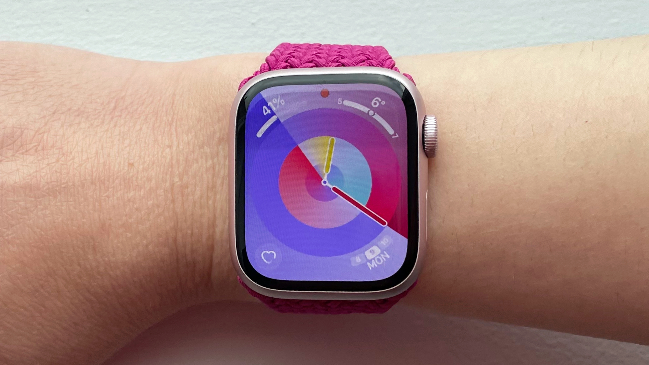 A magenta-colored Apple Braided Solo Loop is attached to a light pink Apple Watch , facing forward on the wearer's wrist.