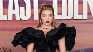 Florence Pugh wearing a black gown and bold jewelry while posing at the "East Of Eden" Screening at BAFTA