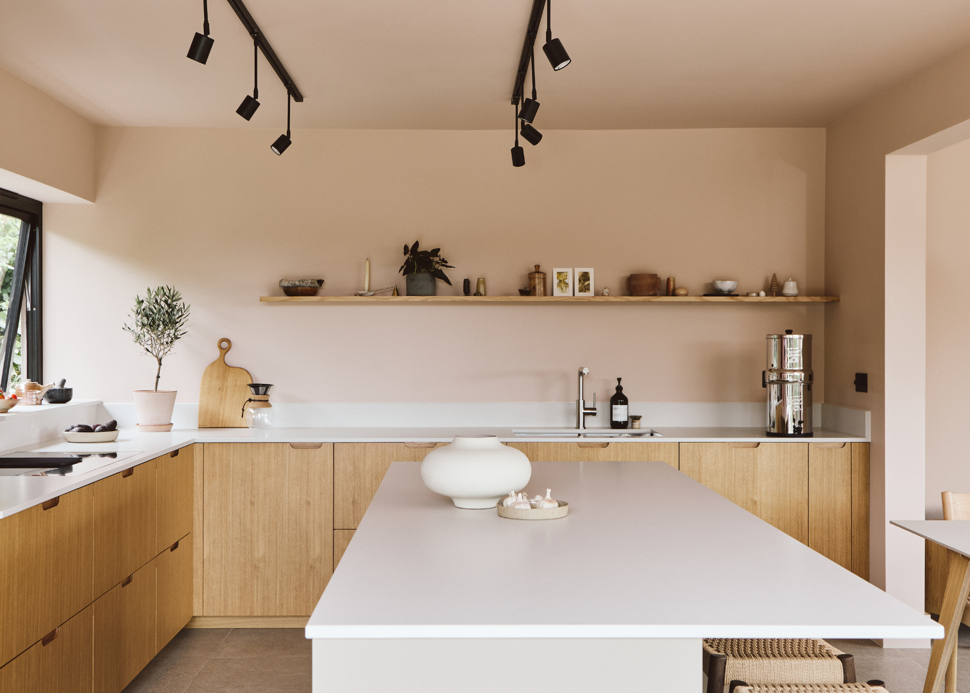 a light neutral kitchen with pink walls wooden cabinets and a white island