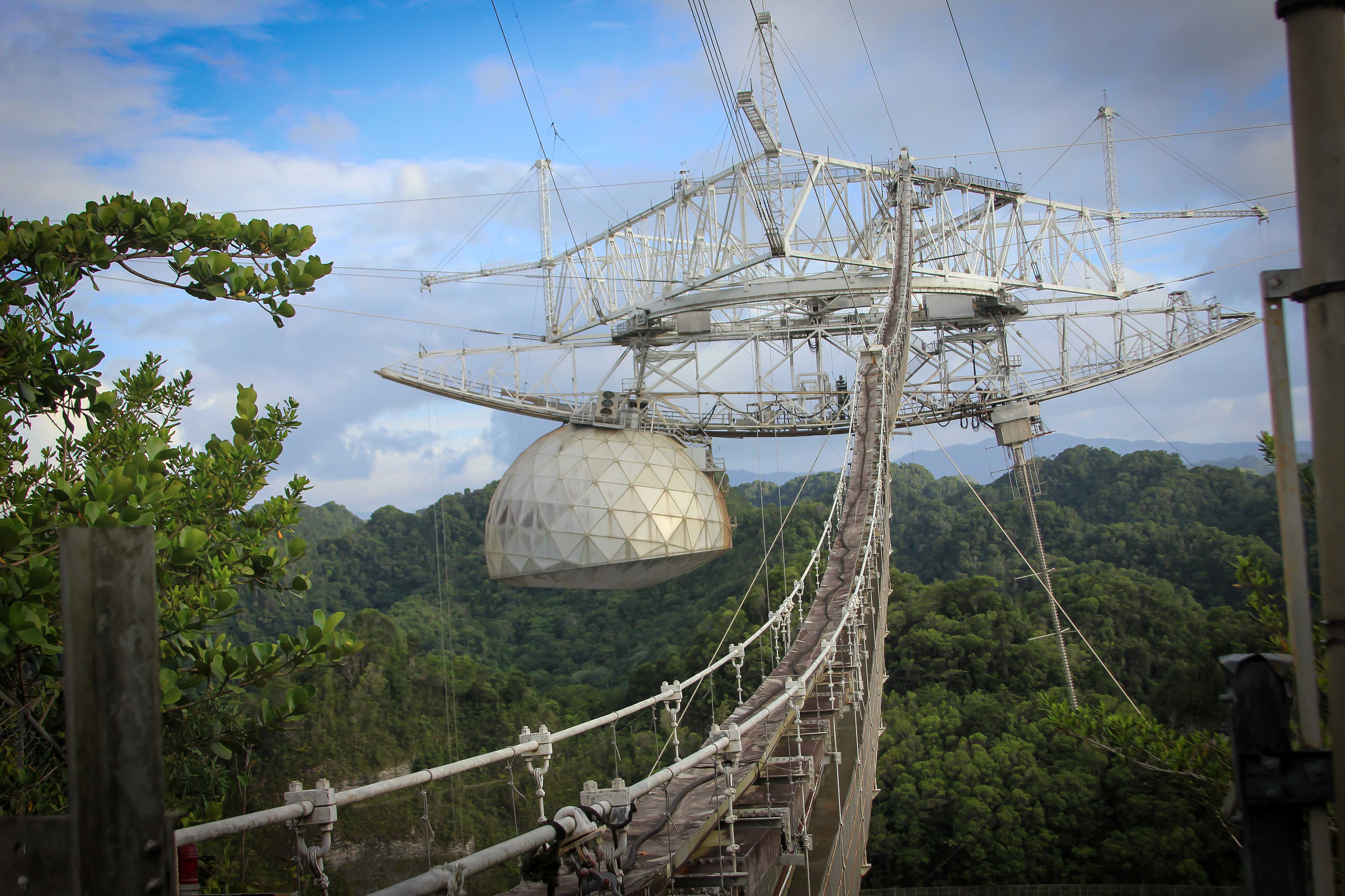 An image of Arecibo Observatory's iconic radio telescope before damage that began in August 2020; the curved azimuth arm and the dome suspended from it are both visible.