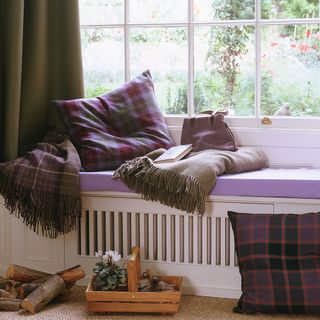 Window seat, tartan blanket, cushions, wooden basket containing wood logs, garden towel and potted plant.