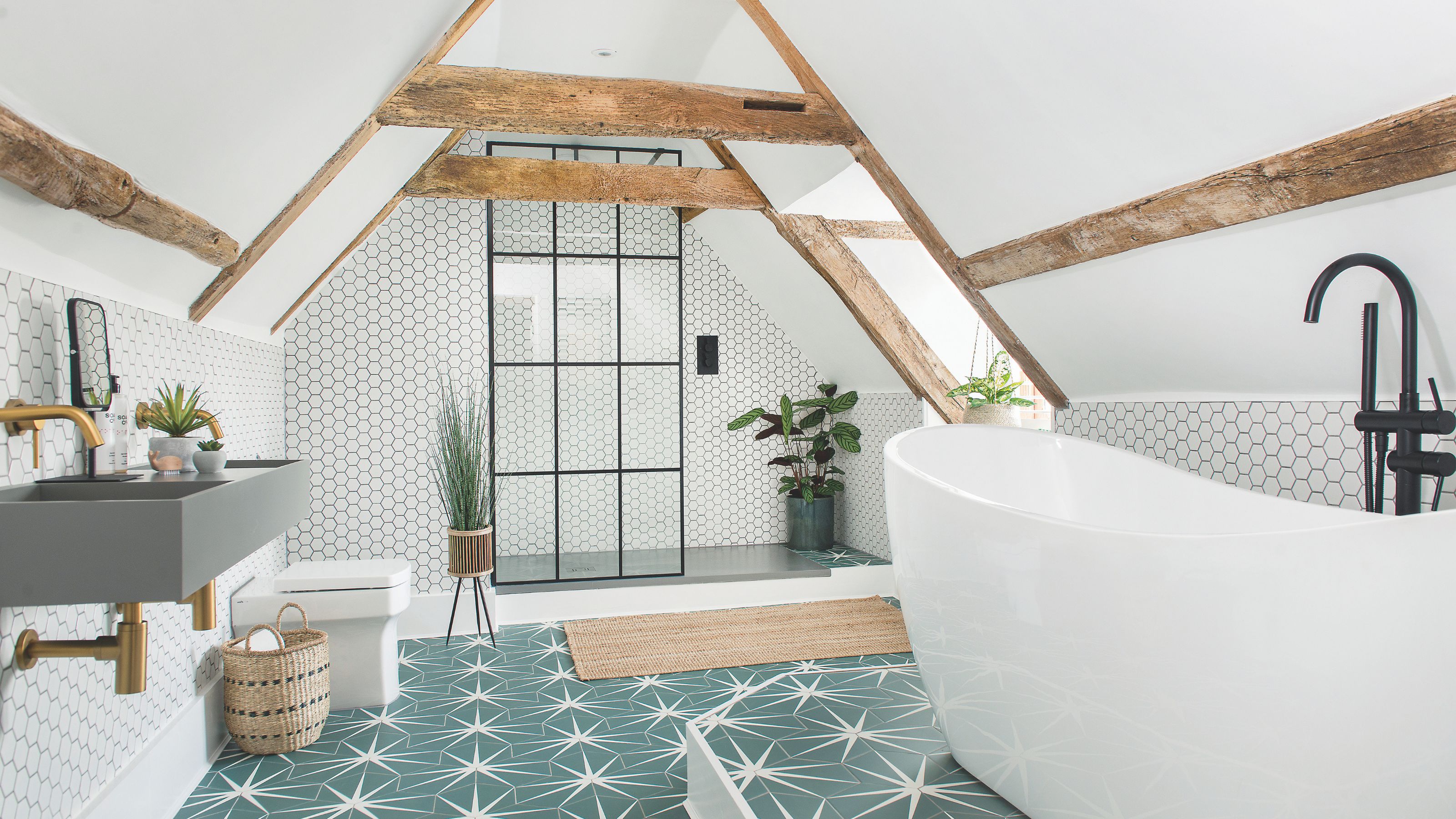 Loft bathroom with exposed beams, green star tiles on the floor, a white freestanding bath and a shower area