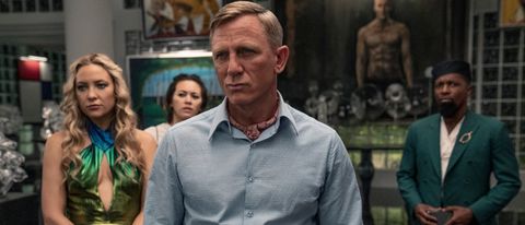 Kate Hudson, Jessica Henwick, and Leslie Odom Jr. standing behind Daniel Craig in Glass Onion: a Knives Out mystery.