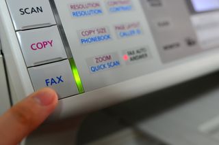 A person pushing the fax button on an old fax machine