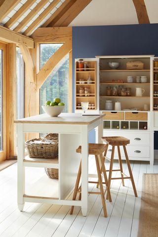 farmhouse style kitchen with blue accent wall, white kitchen island, white floorboards, kitchen dresser, rustic beams
