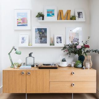 Mid century sideboard against white wall with open shelves and white picture frames