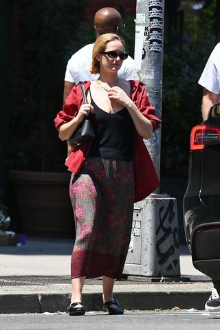 Jennifer Lawrence vestindo camisa vermelha, camisola preta, saia midi estampada e sapatilhas Alaïa Mary Jane cruzadas de couro preto em Nova York.