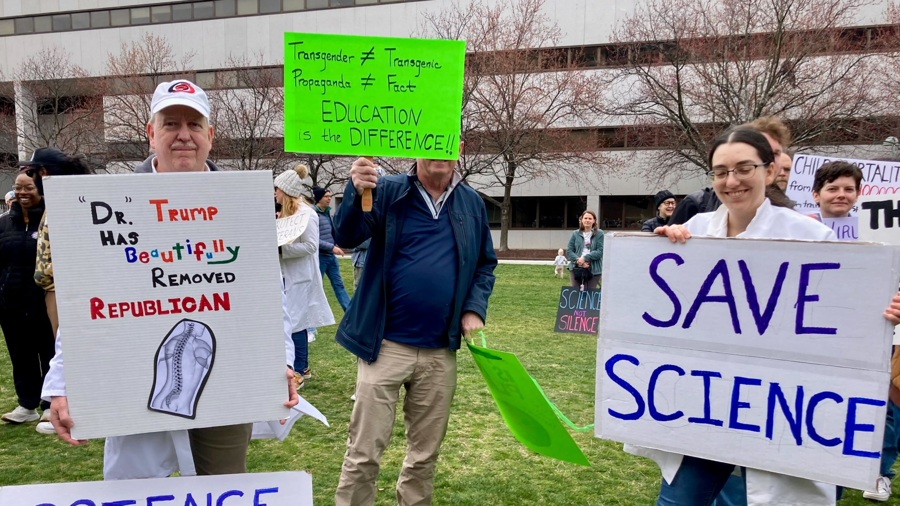 Tembakan poster dan pemrotes di Stand Up For Science Rally di Raleigh; Tiga orang memegang tanda pro-sains.