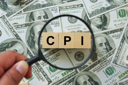 CPI written on wooden blocks under magnifying glass on top of 100 dollar bills