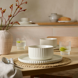 Mabel dinner set on a wood dining table with glasses and a pink vase