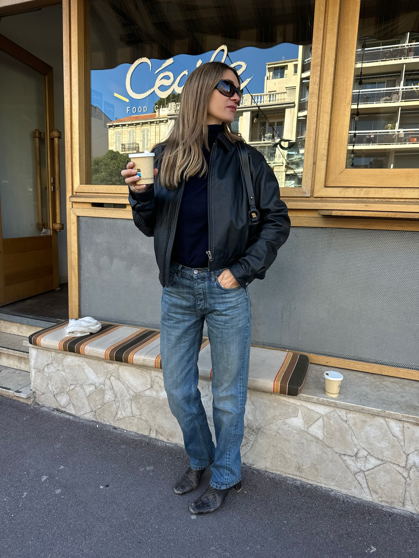 An image of an influencer wearing a black leather jacket, mid-wash jeans and black leather boots, carrying a small black handbag in France