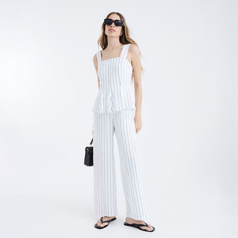 A woman in a peplum white jumpsuit from River Island stands against a white background
