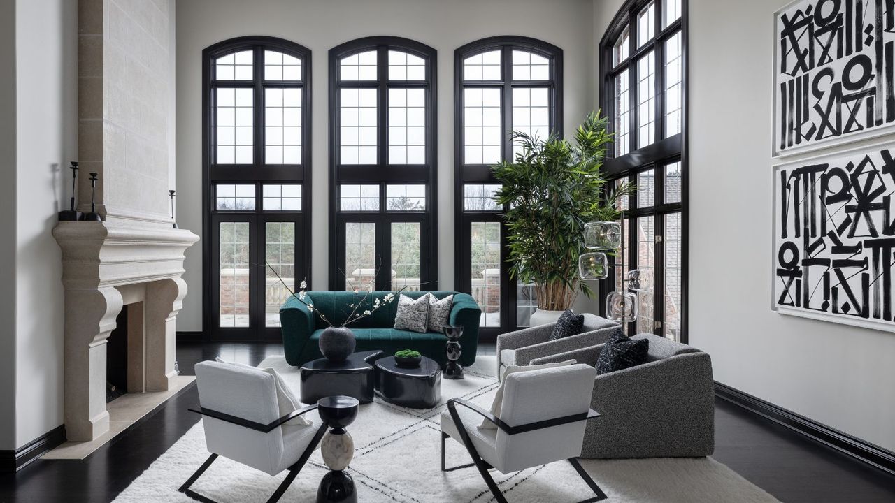 A bright white, modern living room with large windows with black window frames, black and white art, a large statement fireplace and plush modern furnishings