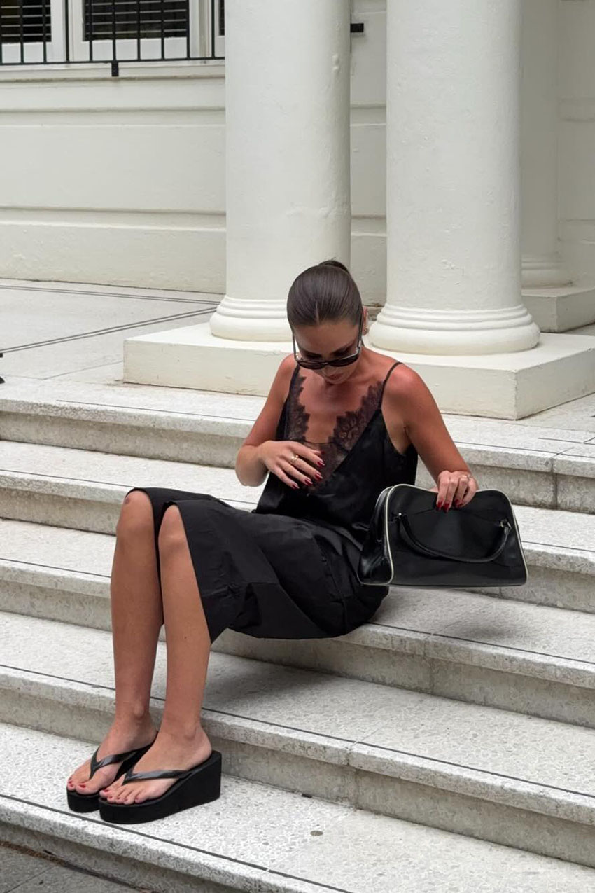 a woman wearing a black dress, black shoulder bag, and black wedge jelly sandals