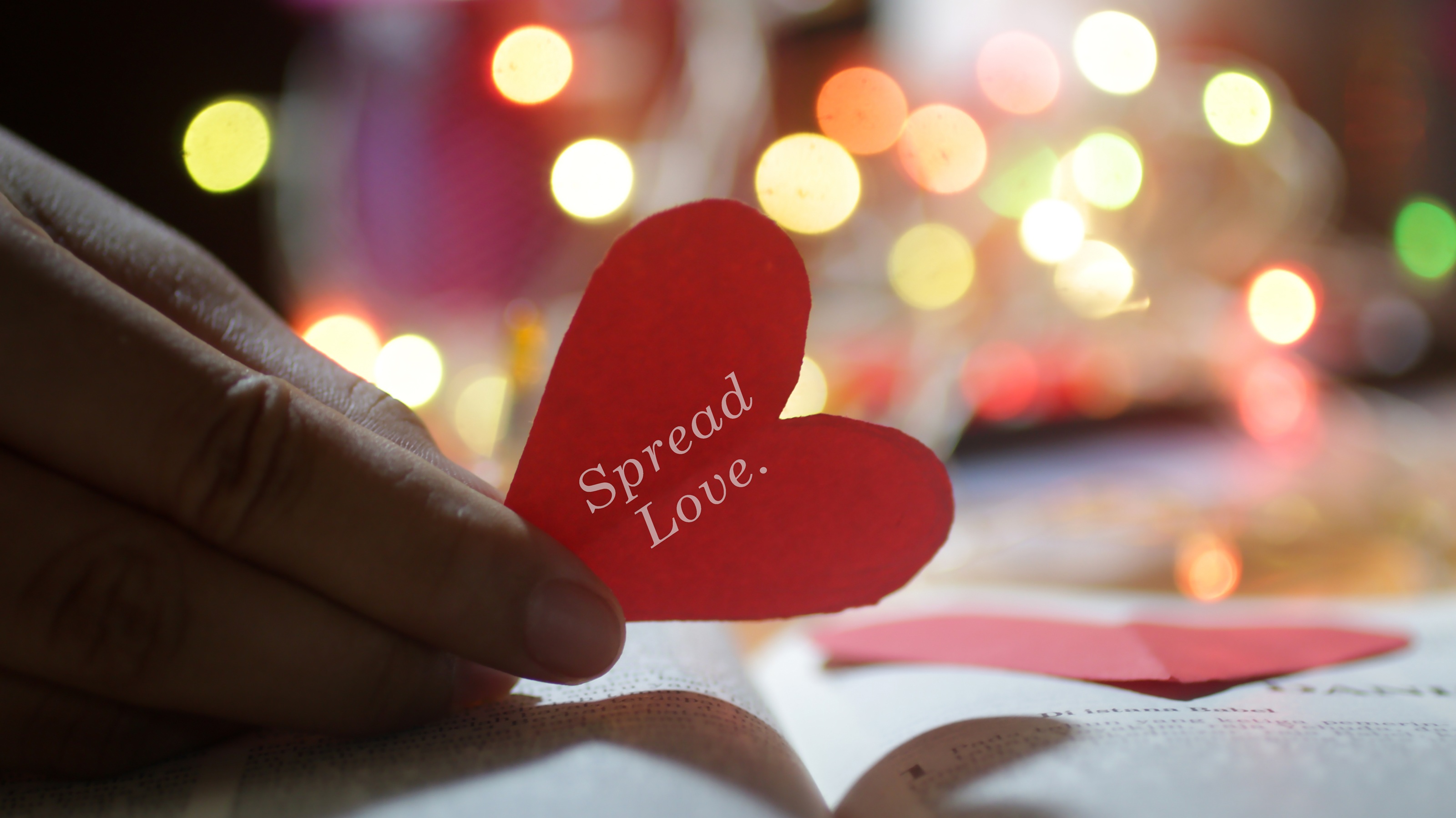 A red paper heart that reads "Spread Love" against the background of holiday lights.