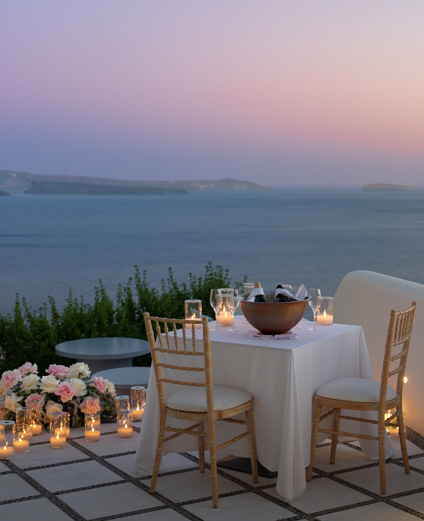 A table by the sea set with candles and wine and pink flowers