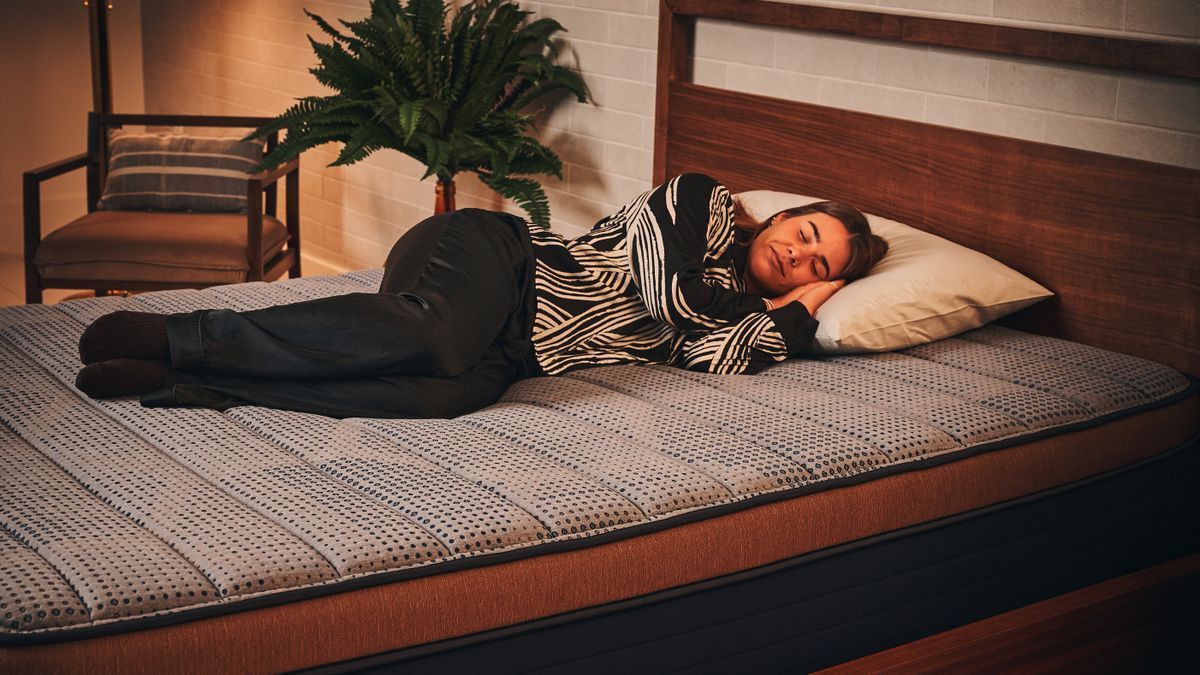 Our mattress tester in white and black silk pyjamas laying on her side on the Brooklyn Bedding Copperflex Memory Foam Mattress on wooden bed frame in sleep studio.