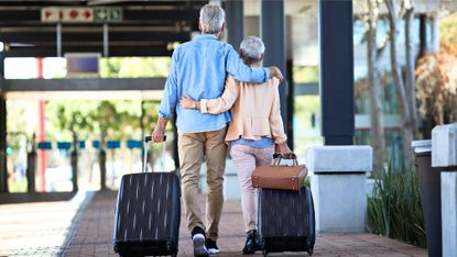 A couple walking into an airport dragging their luggage