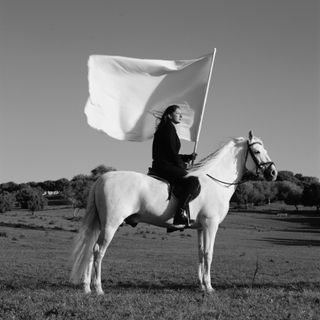 Marina Abramović on a white horse holding a flag