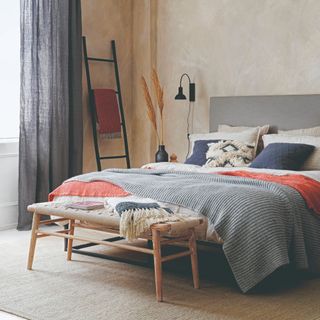 A neutral bedroom painted in a limewash-effect beige shade with pops of coral through soft furnishings