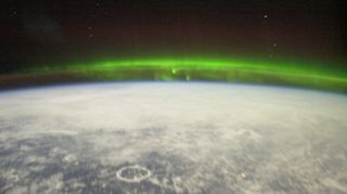 A photo of a green aurora with a crater visible in the foreground