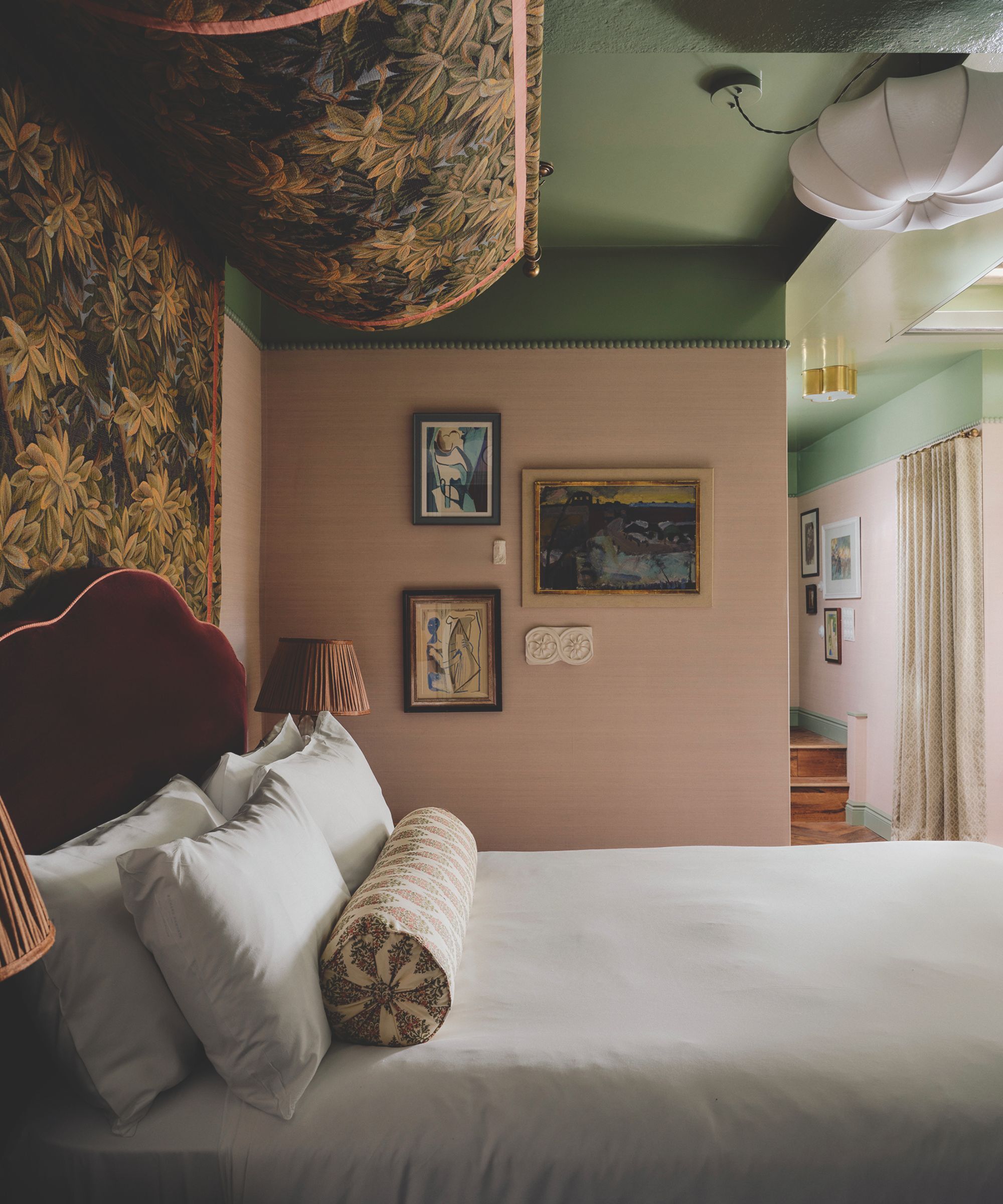A traditional pink and red hotel bedroom with a velvet headboard and white bedding