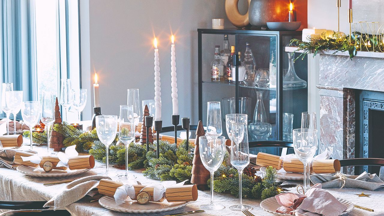 A dining room with a set table decorated for Christmas with candles, crackers and glassware