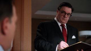 Nathan Lane writing on a notepad and raising his eyebrow while looking down on The Good Wife.