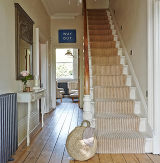 Hallway with wooden floor and white stair case with neutral stair case runner next to woven basket